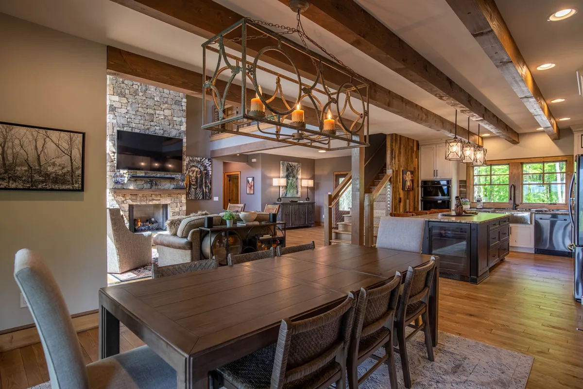 The image captures an open-concept space where the dining area, kitchen island, statement chandelier, and a glimpse of the fireplace come together. The generous dining table is set beneath an elegant chandelier, and nearby, the kitchen island invites both cooking and conversation. The overall mood is lively and communal, ideal for gatherings and festive meals.
