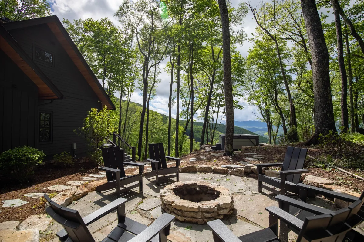 A cozy outdoor fire pit area with comfortable seating, nestled among trees and overlooking the mountains. The scene evokes warmth and camaraderie, ideal for evening gatherings, storytelling, and stargazing as the sun sets.