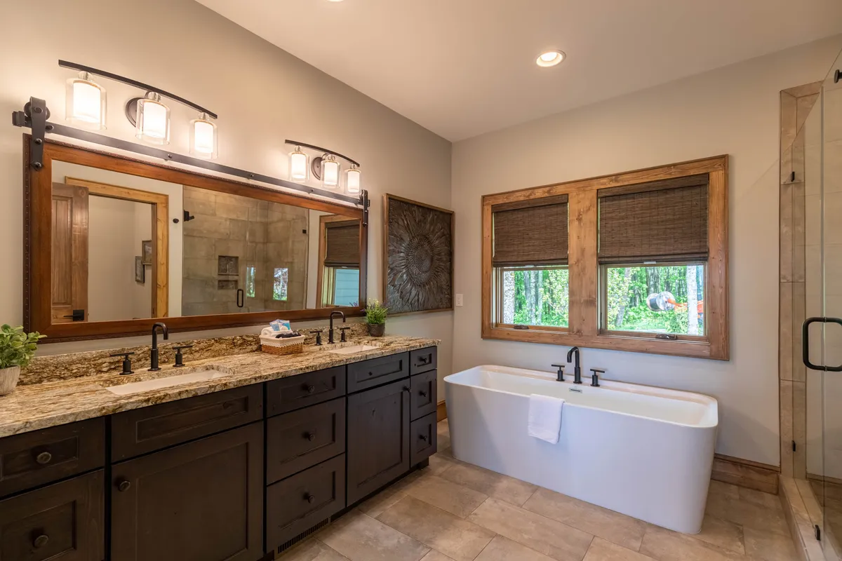 A calm, spa-inspired bathroom featuring a freestanding bathtub, double sink vanity with granite countertops, large mirror, and a framed window letting in natural light. The space exudes luxury and relaxation, perfect for unwinding in a soaking tub or preparing for the day.