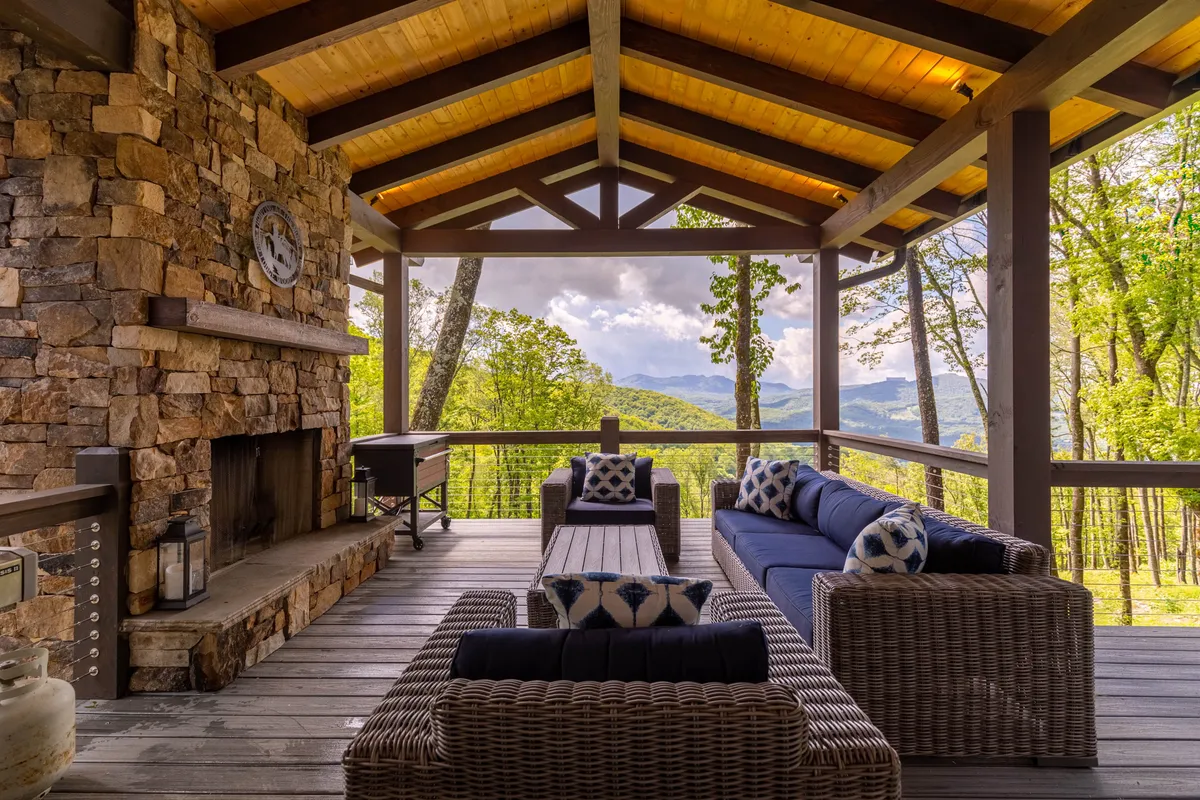 An outdoor stone fireplace set against a stunning mountain view, surrounded by comfortable seating with decorative pillows. The sky stretches wide overhead, creating an ideal spot for socializing, enjoying nature, or stargazing at night.