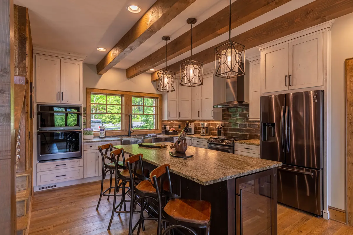 This image offers a closer look at the chef-inspired kitchen, with a central island featuring a granite countertop, modern appliances, wooden ceiling beams, and stylish hanging light fixtures. The open layout allows for effortless entertaining and culinary creativity.