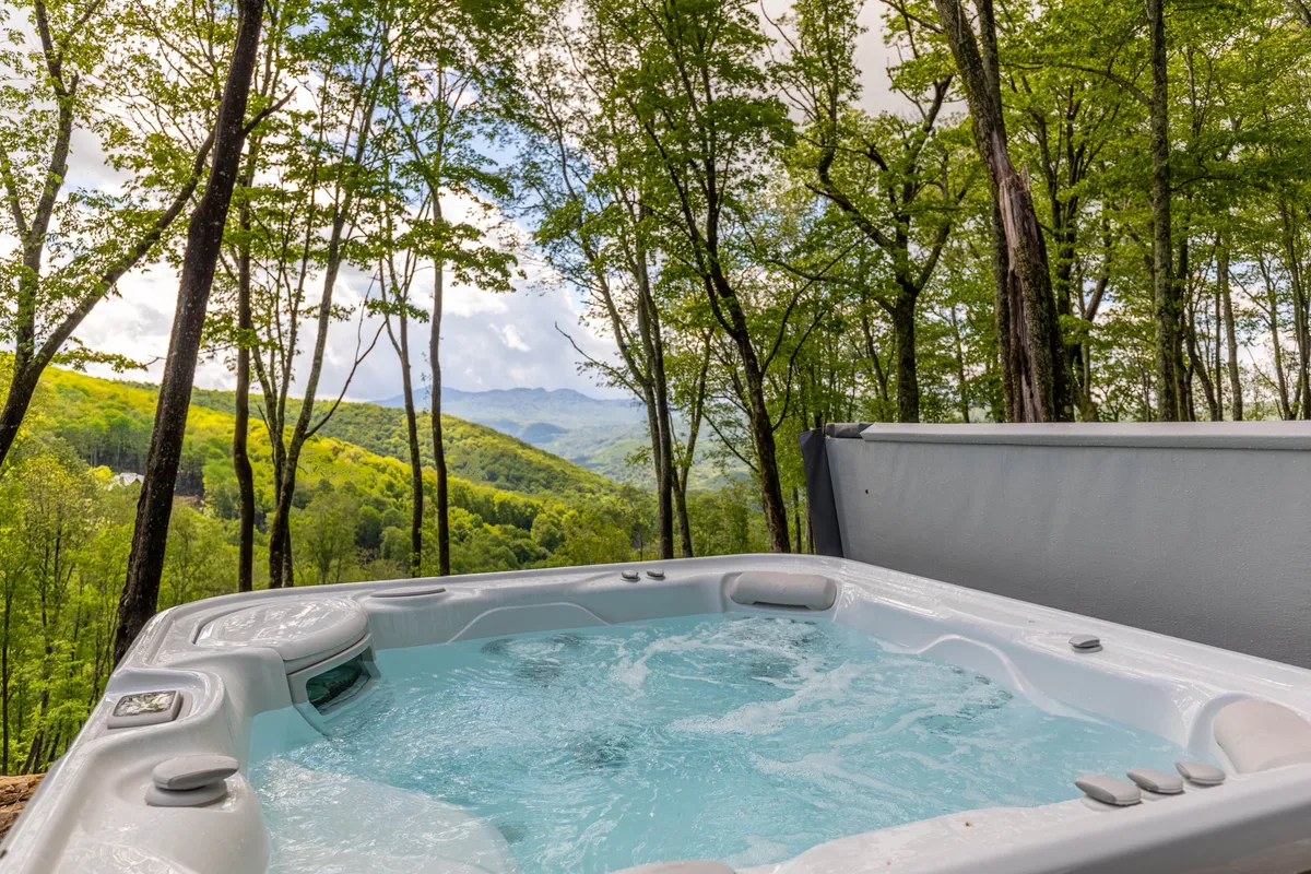 Nestled among trees, a bubbling hot tub offers a front-row view of the surrounding mountains. The scene exudes tranquility, with the hot tub perfectly positioned for stargazing or soaking in sunset colors.