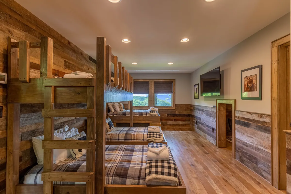 This cozy bunk room features wooden bunk beds, warmly lit by large windows and surrounded by decorative pictures on the walls. The space is clearly designed for kids, with a welcoming, playful ambiance that hints at sleepovers and imaginative play.