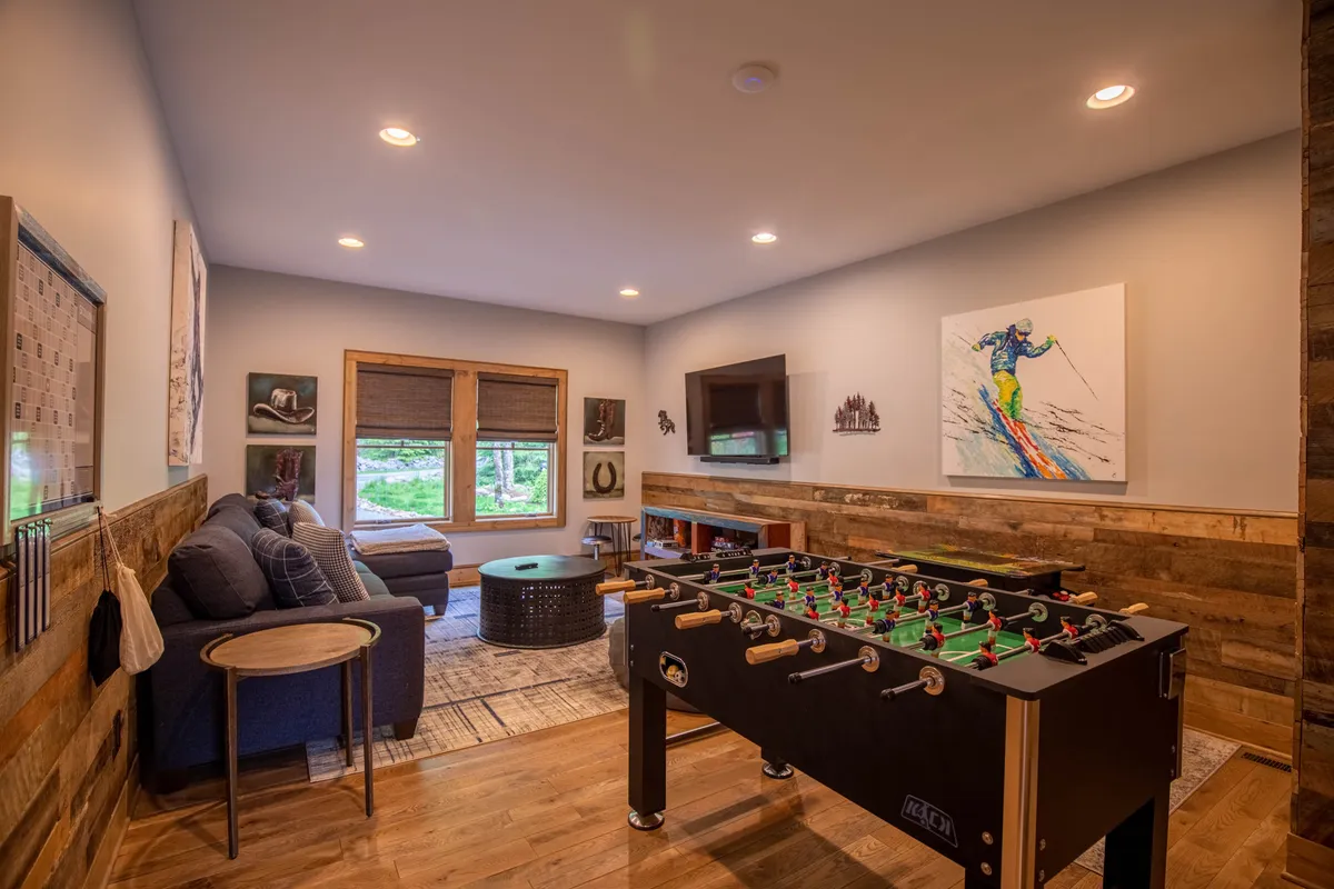 This image features a vibrant game room with a foosball table, a comfortable couch, artwork on the wall, and a television. The layout encourages both energetic play and relaxed socializing, perfectly capturing the essence of a family fun zone.